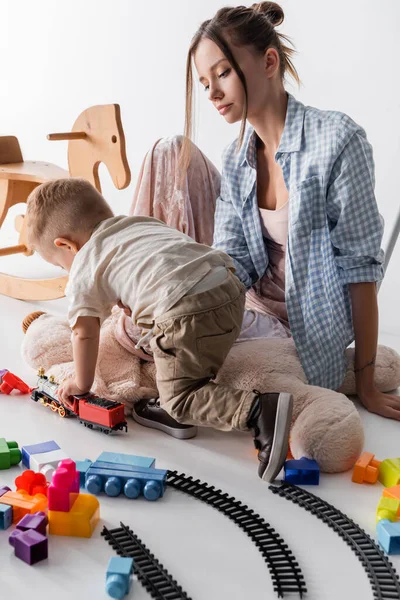 Little boy playing with toy train near mother on white — Stock Photo