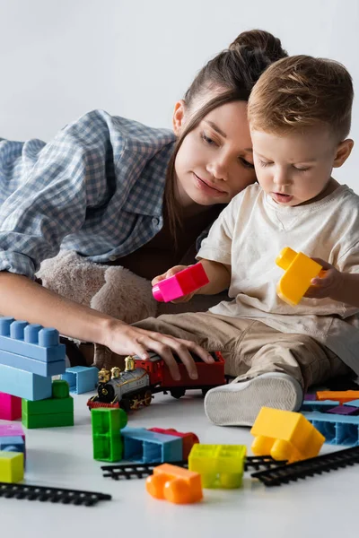 Mère et enfant jouant avec des cubes de construction et chemin de fer jouet sur gris — Photo de stock