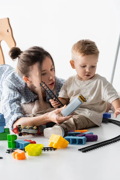 Jovem mulher com pequeno filho brincando com brinquedo ferroviário no branco — Fotografia de Stock