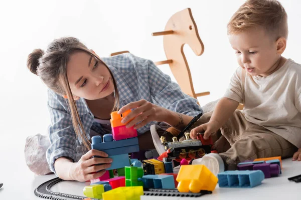 Mutter und Sohn spielen mit Bauklötzen und Spielzeugeisenbahn auf weiß — Stockfoto