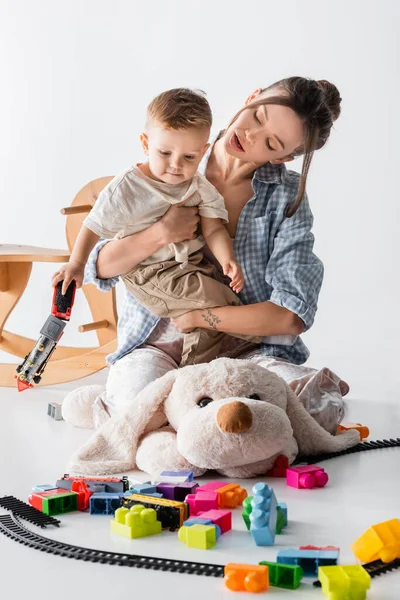 Woman hugging baby boy while sitting on large toy dog on white — стоковое фото