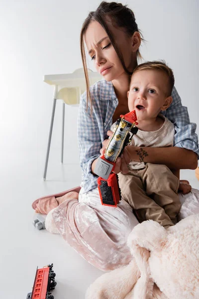 Exhausted woman embracing amazed son holding toy train on white — Photo de stock