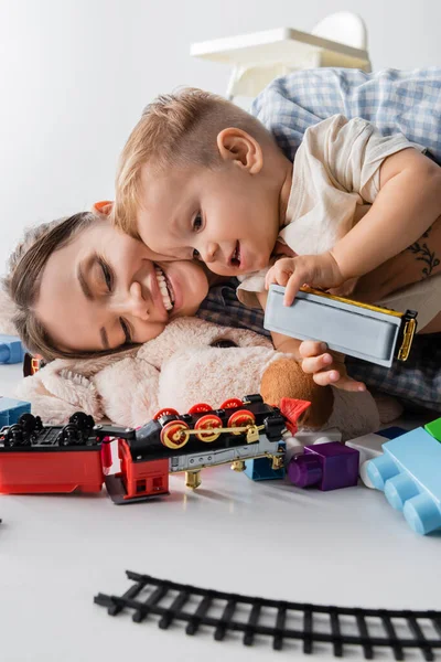Щаслива жінка лежить з веселим сином біля іграшок на білому — стокове фото