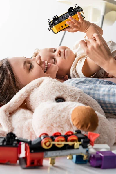 Happy woman and boy with toy train lying near blurred soft toy isolated on white — Foto stock