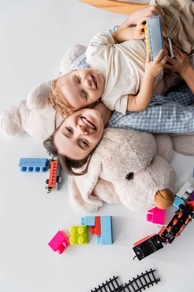 Top view of cheerful woman and toddler son lying on huge soft toy on white — Photo de stock