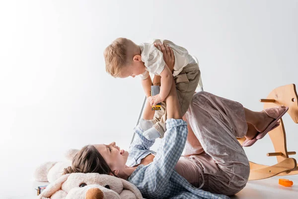 Alegre mujer acostado en juguete perro y jugando con niño hijo en blanco - foto de stock