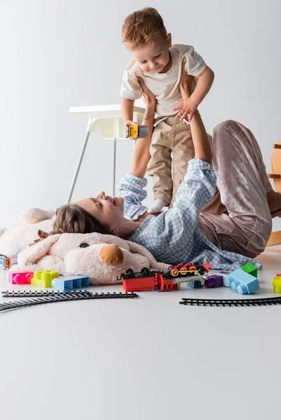 Happy woman holding little son while lying on toy dog on white — Stock Photo