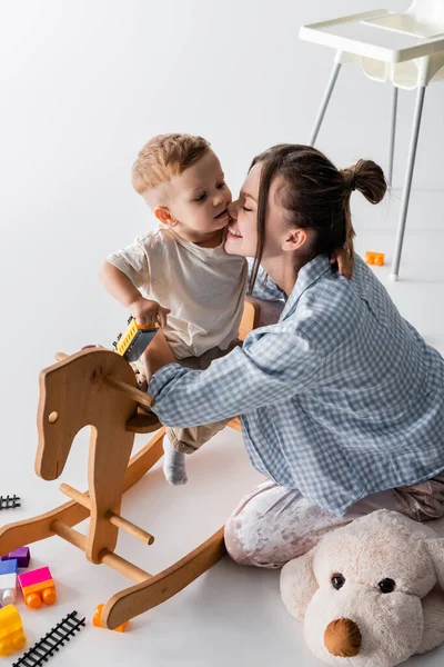 Happy woman hugging son sitting on rocking horse on white — Foto stock