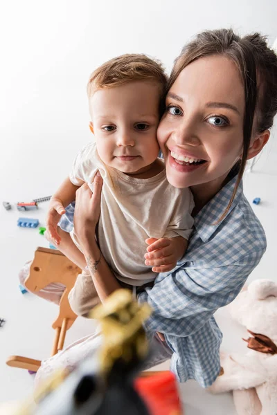 Cheerful woman looking at camera while hugging toddler boy on white — Foto stock