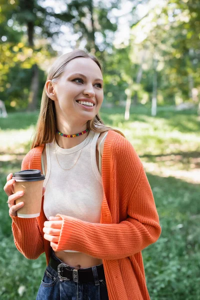 Mulher sorrindo segurando copo de papel com café para ir no parque verde — Fotografia de Stock