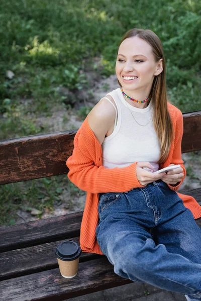 Щаслива жінка тримає смартфон і сидить на лавці — стокове фото