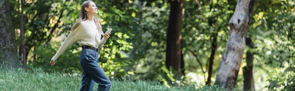 Feliz joven con teléfono inteligente caminando en el parque, bandera - foto de stock