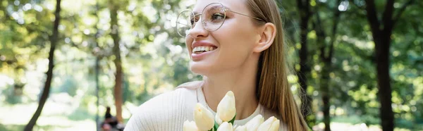 Donna allegra in occhiali sorridente vicino a tulipani in parco, stendardo — Foto stock