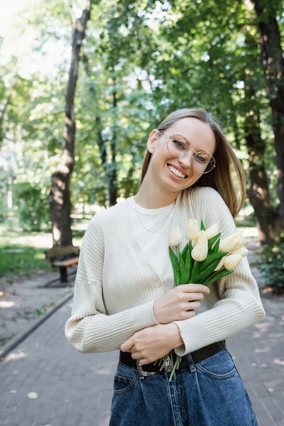 Happy woman in glasses holding bouquet of tulips in green park — Stock Photo