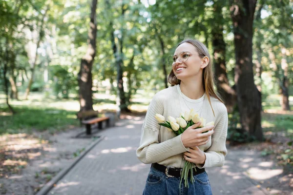 Femme heureuse dans des lunettes tenant bouquet de tulipes dans le parc vert — Photo de stock