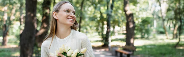 Щаслива жінка в окулярах тримає букет тюльпанів в парку, банер — стокове фото