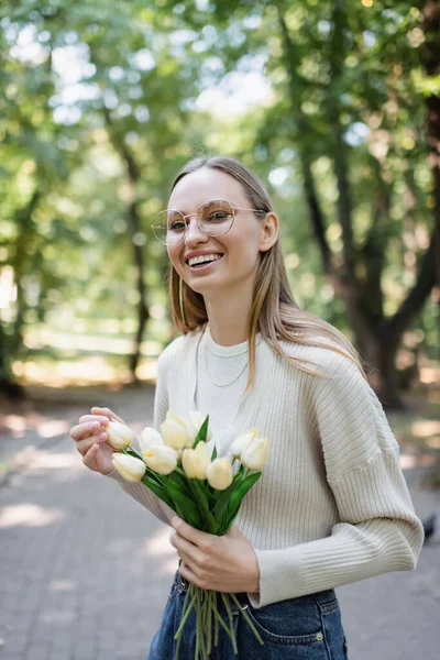 Donna allegra in occhiali che tengono il mazzo di tulipani in parco verde — Foto stock