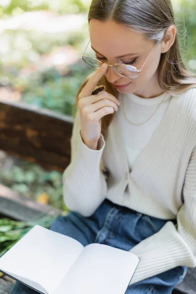 Woman adjusting glasses while holding blank notebook and pen — Photo de stock