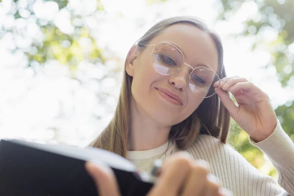 Low angle view of smiling woman in glasses holding blurred notebook — Photo de stock