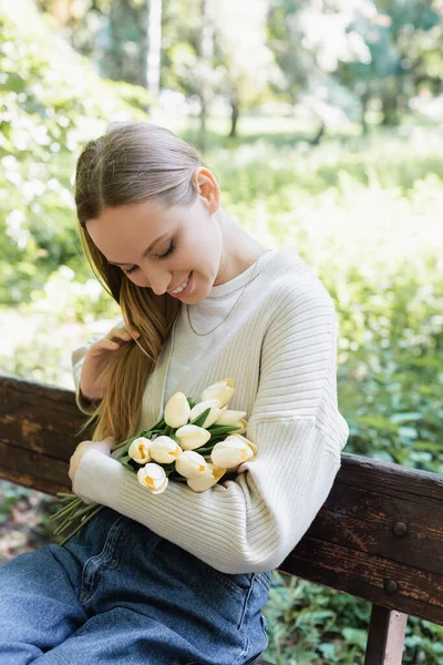 Happy woman looking at bouquet of blooming tulips in park — Stock Photo