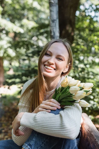 Femme heureuse tenant des tulipes en fleurs dans un parc vert — Photo de stock