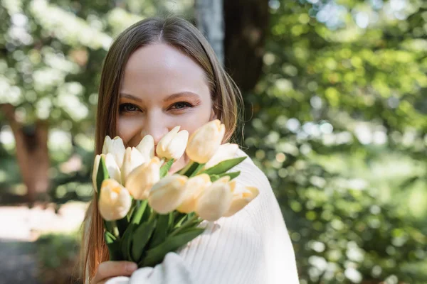Frau bedeckt Gesicht, während sie blühende Tulpen im grünen Park hält — Stockfoto