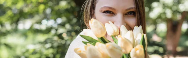 Frau bedeckt Gesicht, während sie blühende Tulpen im Park hält, Banner — Stockfoto