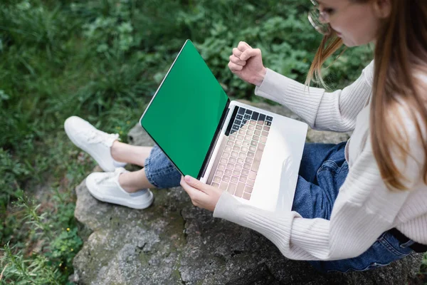 Vista de alto ângulo da mulher feliz usando laptop com tela verde enquanto sentado em pedra — Fotografia de Stock