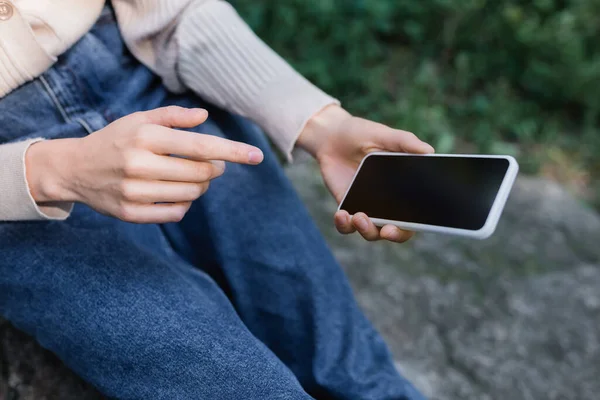 Cropped view of woman in jeans pointing with finger at smartphone with blank screen — Stock Photo