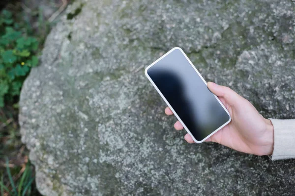 Vista cortada de mulher segurando smartphone com tela em branco contra pedra — Fotografia de Stock