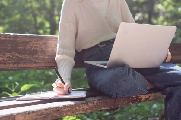 Ausgeschnittene Ansicht einer Frau mit Laptop beim Schreiben im Notizbuch — Stockfoto