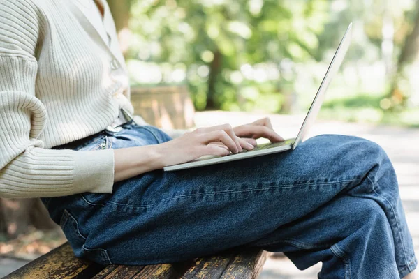 Cropped view of woman using laptop while sitting on bench — Stock Photo