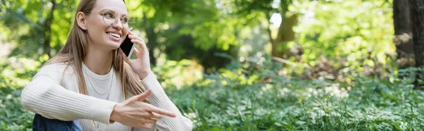 Joyful woman in glasses talking on smartphone in green park, banner — Stock Photo