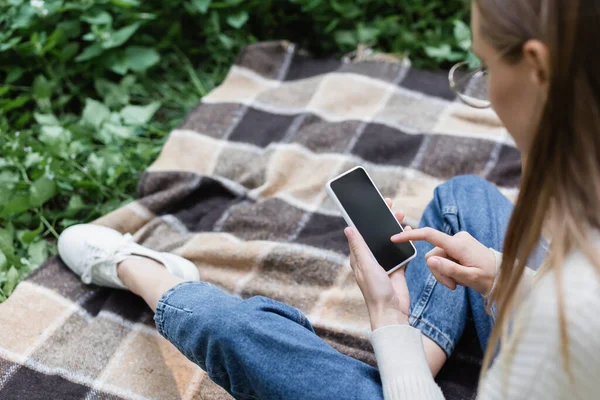 High angle view of woman in glasses using smartphone with blank screen while sitting on checkered plaid — Fotografia de Stock