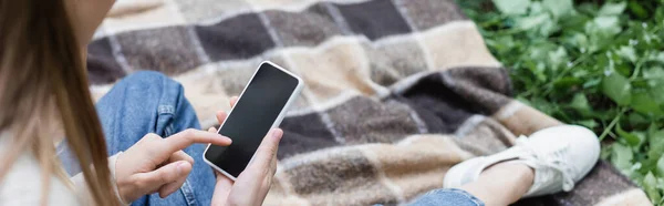 Cropped view of woman using smartphone with blank screen while sitting on checkered plaid, banner — Fotografia de Stock