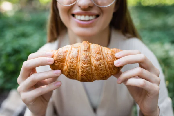 Vista cortada de mulher feliz sorrindo e segurando delicioso croissant — Fotografia de Stock