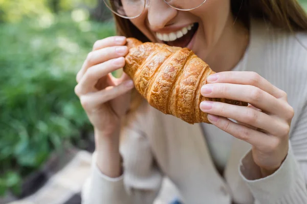 Cropped view of happy woman holding biting croissant - foto de stock