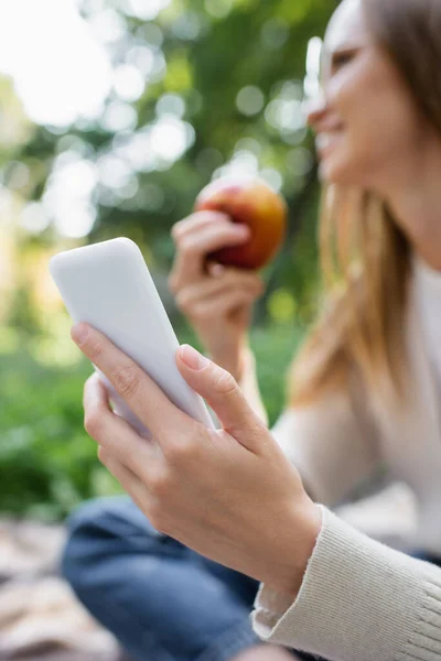 Blurred woman holding apple and smartphone in hands — Stock Photo