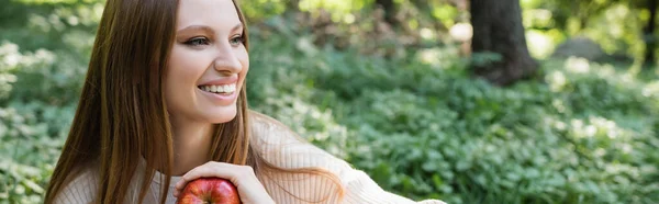 Веселая женщина с красным вкусным яблоком в зеленом парке, баннер — стоковое фото