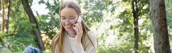 Donna felice in occhiali avendo telefonata su smartphone in parco verde, banner — Foto stock