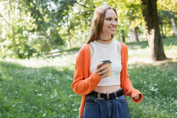 Cheerful woman in orange cardigan holding takeaway drink in paper cup — Stock Photo