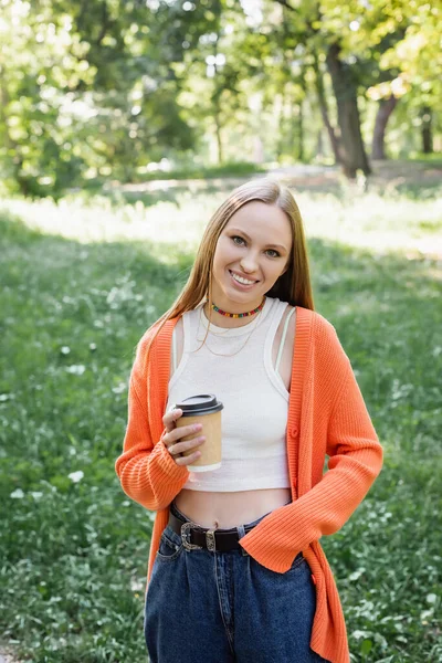 Positive woman in orange cardigan holding takeaway drink in paper cup — Stock Photo