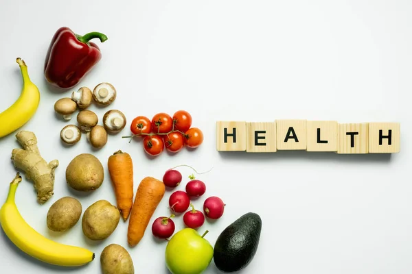 Draufsicht auf Holzwürfel mit Gesundheitsschriftzug in der Nähe von Lebensmitteln auf weißem Hintergrund — Stockfoto