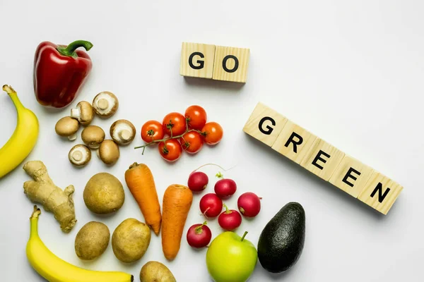 Top view of organic food and wooden cubes with go green lettering on white background — Fotografia de Stock