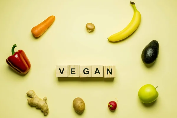 Top view of cubes with vegan lettering near fresh food on yellow background — Fotografia de Stock