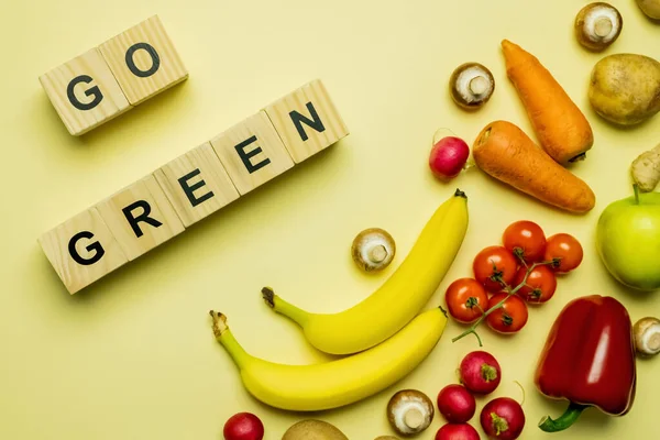 Top view of cubes with go green lettering near fresh food on yellow background — Stockfoto