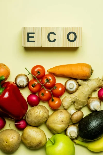 Top view of wooden cubes with eco lettering near organic food on yellow background — Photo de stock