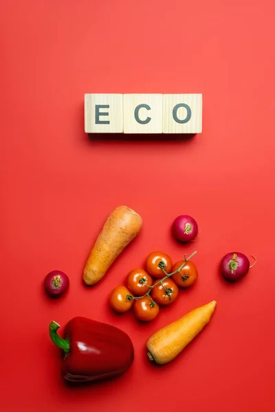 Top view of eco lettering on wooden cubes near fresh vegetables on red background — Stockfoto