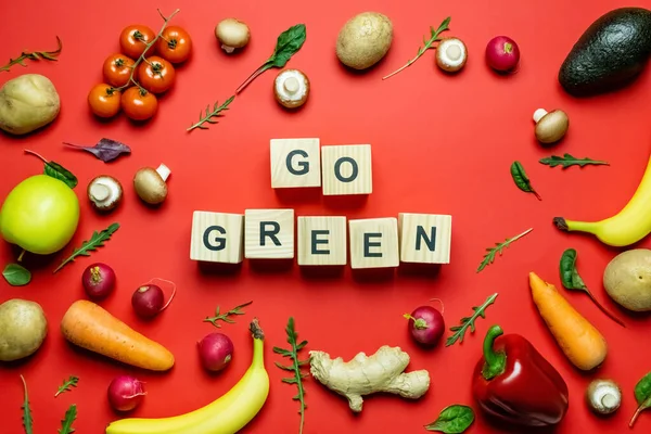 Puesta plana de comida fresca y letras verdes en cubos sobre fondo rojo - foto de stock