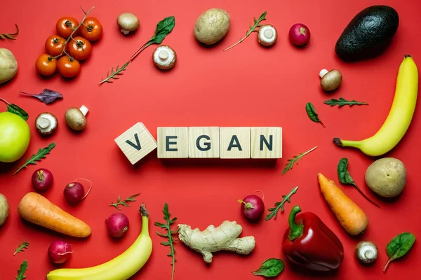 Flay mit veganem Schriftzug auf Holzwürfeln in der Nähe von reifem Gemüse und Obst auf rotem Hintergrund — Stockfoto